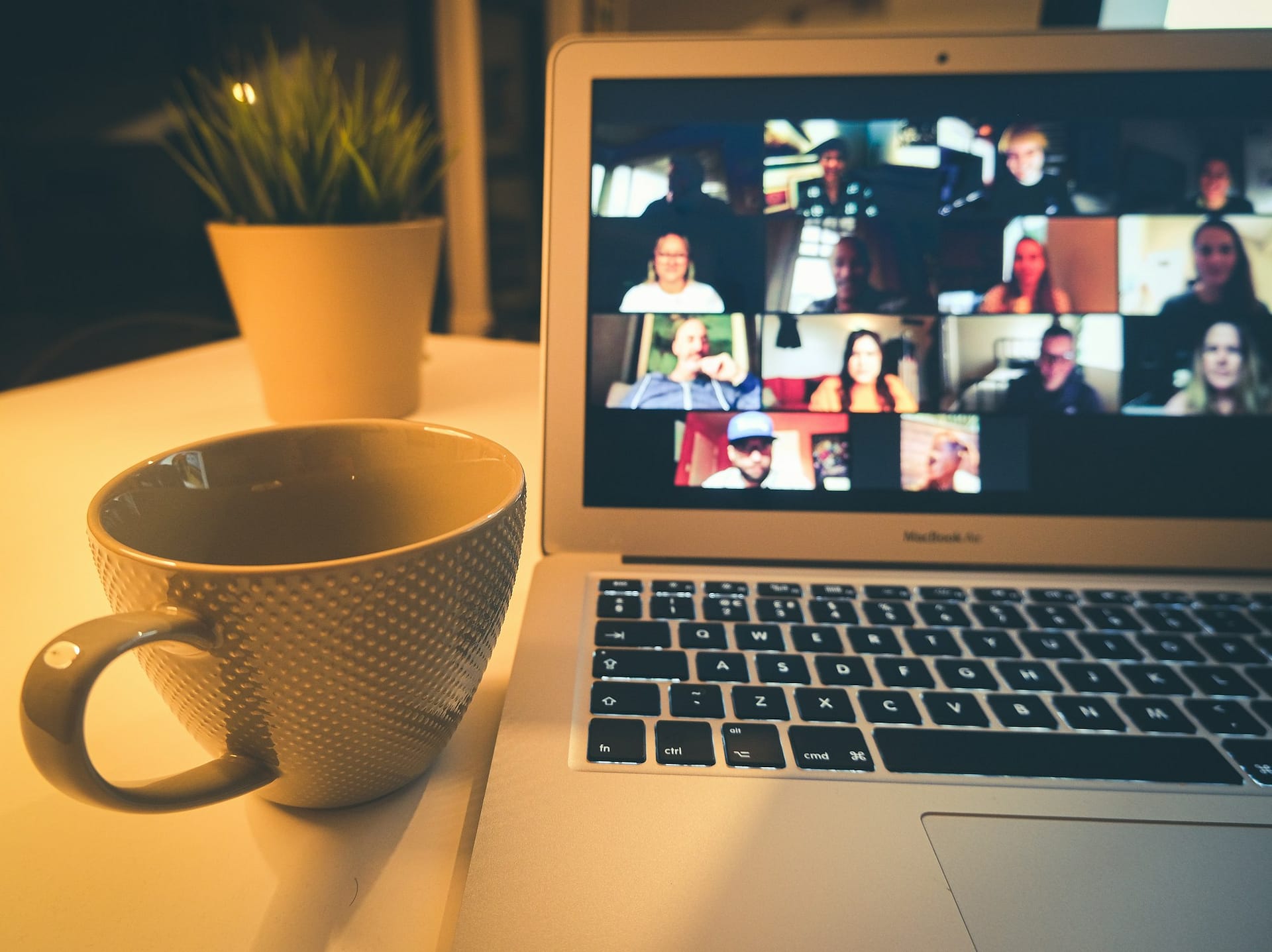 A laptop showing a video call beside a cup of coffee